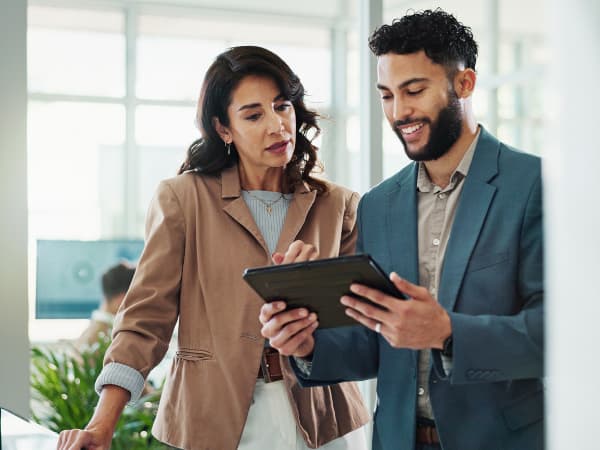 Two business professionals in an office reviewing information together on a tablet device.